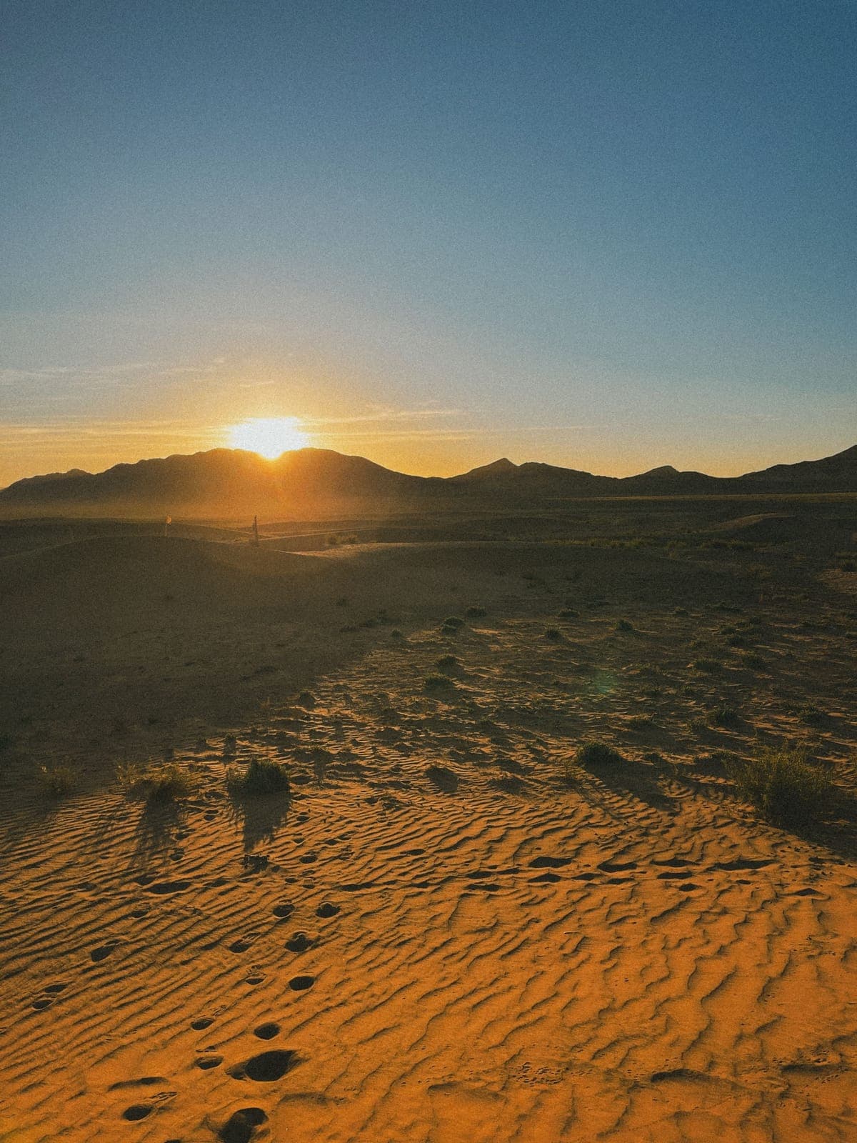 Sunrise over sand dunes with footprints in the desert