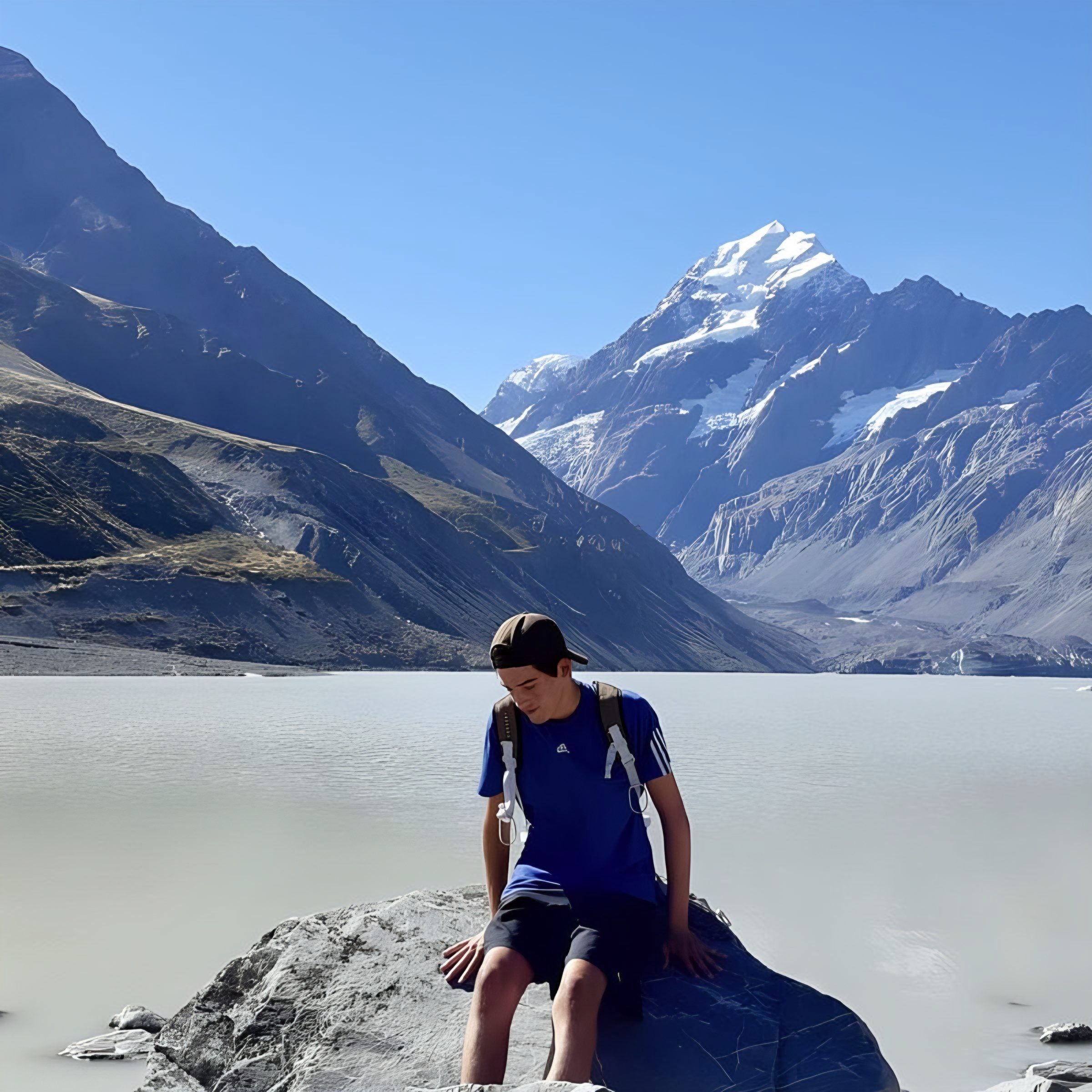 Erik sitting on a rock by a glacier lake in front of snow-capped mountains in New Zealand